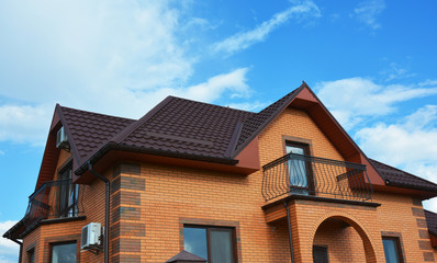 Valley and gable brick house roofing construction with attic windows, roof gutter, metal roofing and metal balcony. Roof gutter system, skylight window on attic house metal tiles roofing