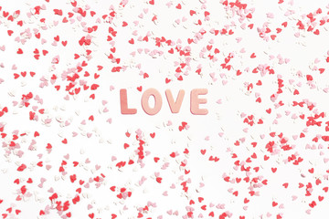 Word Love made of wooden letters. Pattern made of colorful hearts on a white background