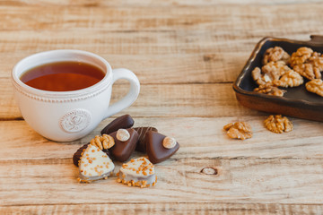 Fototapeta na wymiar Cup of hot black tea with chocolate candy and walnuts on wooden table, selective focus.