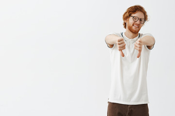 Totally dislike. Portrait of dissatisfied and uninterested unhappy redhead male model with beard and messy hairstyle turning head from camera from disgust and disappointment showing thumbs down