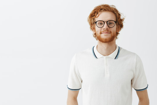 Waist-up shot of friendly good-looking happy guy with ginger hair and beard smiling carefree and gazing with optimistic and calm expression at camera having faith in good day over gray background