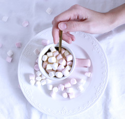 Valentines composition. Woman's hand and cup of hot chocolate with Marshmallows, on white table background. Winter breakfast concept. Flat lay, top view.