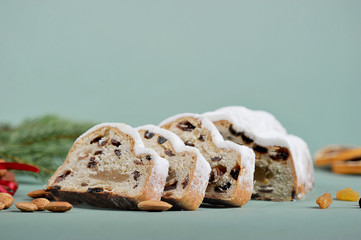 Slices of Christmas stollen. The frame space is occupied by slices of cake, cinnamon sticks, raisins and almond nuts. Light gray background. Close-up. Macro shooting. Free space under the text.
