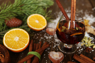 mulled wine or hot tea in a glass with two sticks of cinnamon and spices on a wooden background with heart-shaped cookies, with a spruce twig closeup. Christmas composition or background.