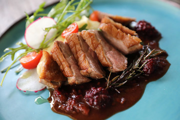 Duck confit with salad , baked apple and raspberry sauce served on wooden table