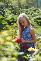 Portrait of a long haired litter girl in flowers. Summer flowers. Summertime moments. Roses and a little blond girl in blue dress.