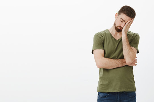 Oh gosh how tiresome. Portrait of tired and drained male workaholic with beard leaning on palm as making facepalm sign, close eyes exhausted and drained posing upset and uneasy over white background