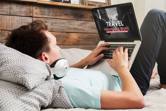 Man visiting a travel agency website by internet with a laptop computer, while lying down on the bed at home.
