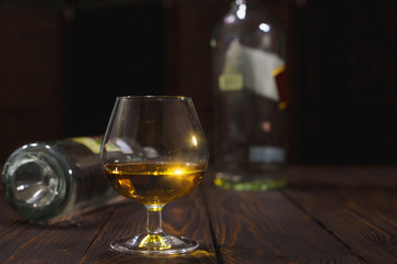 Glass of whiskey or brandy and empty bottles on wooden table