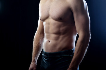 Fototapeta na wymiar Athletic man with strained balanced chest and abdominal muscles on a dark studio background.