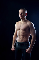 Fototapeta na wymiar Athletic slim trainer showing muscles on a black studio background