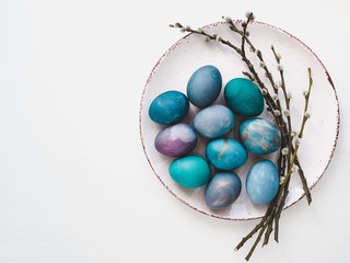 Multi-colored Easter eggs, twigs willows and old, vintage plate on a white background. Top view, close-up, isolated. Preparation for the holiday