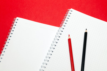 Notepad and red and black pensils blank sheets in cage white paper on spring on red background. Concept of free space, copyspace, business book, diary, use for notes at art seminar, conference