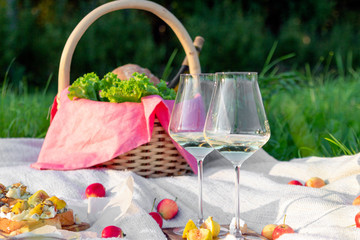 Fototapeta na wymiar Picnic in forest on sunny meadow, blanket, wicker basket, wine glasses, bruschetta with cheese and pear, snacks, fruit, apples, bread. Concept of romantic lunch date in picturesque forest