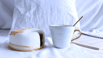 Fototapeta na wymiar Cozy winter morning breakfast in bed still life scene. Steaming cup of hot coffee, tea and yummy cake. Christmas concept. Pillows, and a notebook .