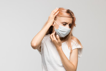 Isolated studio portrait of young beautiful woman with medical mask in white t-shirt scratching...