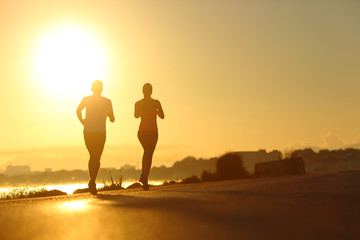 Couple practicing sport running at sunset on the road