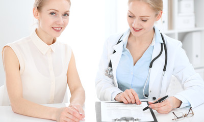 Doctor and patient talking in hospital office while sitting at the desk. Health care and client service in medicine