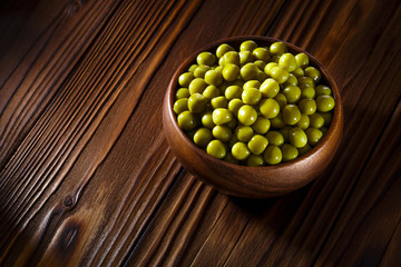 Green peas in a wooden bowl on dark brown wooden table