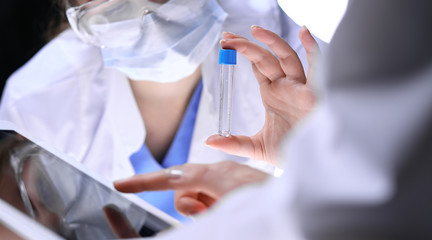 Fototapeta na wymiar Closeup of scientific research team with clear solution in laboratory. Blonde female chemist holds test tube of glass while her colleague checks results with tablet pc. Blood test, medicine or