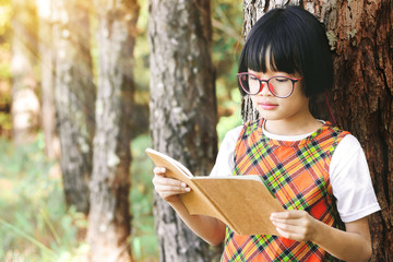 Cute little girl with glasses reading book in the pine forest