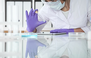 Close-up of professional female scientist in protective eyeglasses making experiment with reagents...