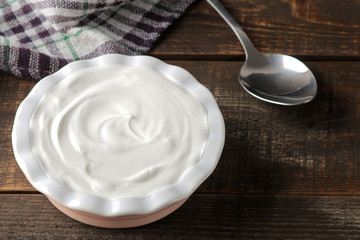 greek yogurt in a ceramic bowl next to a spoon on a brown wooden background