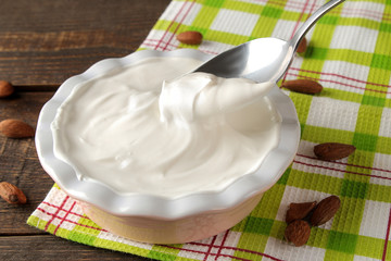 Greek yogurt in a ceramic bowl and with almond nut next to a spoon on a brown wooden background.