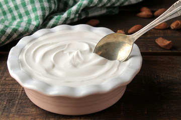 Greek yogurt in a ceramic bowl and with almond nut next to a spoon on a brown wooden background.