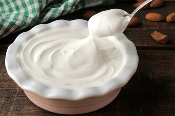 Greek yogurt in a ceramic bowl and with almond nut next to a spoon on a brown wooden background.