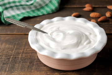 Greek yogurt in a ceramic bowl and with almond nut next to a spoon on a brown wooden background.