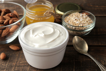 Greek yogurt in a ceramic bowl with almonds and honey, oatmeal next to a spoon on a brown wooden...