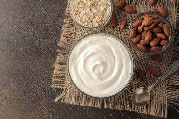 Greek yogurt in a glass bowl next to a spoon, oatmeal and almonds on a dark background. healthy food. natural yoghurt. breakfast. top view with space for text