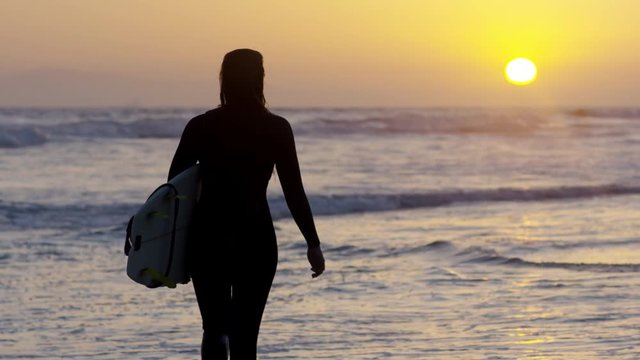 Surfer Carries Her Surfboard And Walks Along Shore, Waves Lap At Her Feet, Beautiful Sunset (Slow Motion)