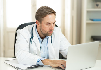 Handsome doctor working on medical expertise and searching information on laptop at hospital office