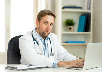 Handsome doctor working on medical expertise and searching information on laptop at hospital office