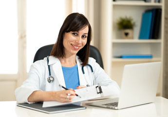 Female doctor working feeling up prescription and medical records with clipboard and laptop office