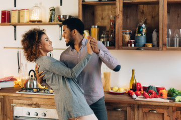 Young african-american couple dancing in kitchen, copy space
