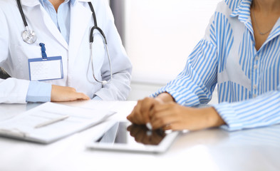 Fototapeta premium Doctor and patient talking and discussing health treatment while sitting at the desk. Physician pointing into tablet pc, close-up. Medicine and health care concept