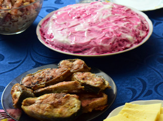 Festive snacks and salad on the table. Fried red fish. Sliced sausage and cheese. Salad herring under fur coat. Russian traditional cuisine.