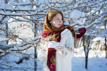 A girl of European appearance in the village stands on the street. Winter outside and frost. Sunny day.
