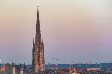 View of Basilica of St. Michael steeple tower with construction cranes in the background at sunset, city of Bordeaux, France