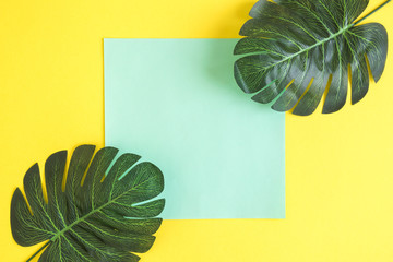 Flat lay of tropical leaves and paper against yellow background