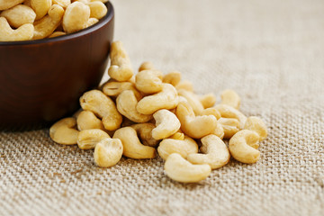 Cashew nuts in a wooden bowl on a burlap cloth background.