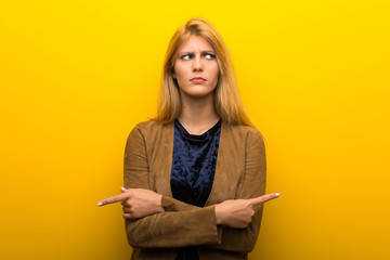 Blonde girl on vibrant yellow background pointing to the laterals having doubts