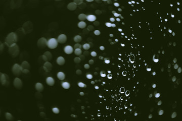Dirty window glass with drops of rain. Atmospheric green background with raindrops in bokeh. Droplets and stains close up. Detailed transparent texture in macro with copy space. Rainy weather.