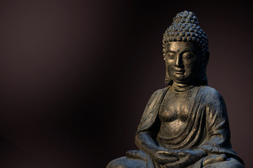 Buddha statue sitting in meditation pose against deep dark background.