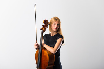 Young blonde girl with her cello posing on white wall © luismolinero
