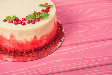 close up of white cake decorated with currants and mint leaves on pink surface
