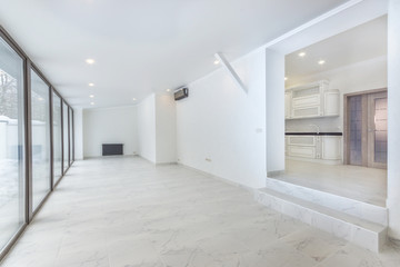Empty white room with tiled floor and floor to ceiling window. Sliding doors to the back yard. Large doorway to the kitchen